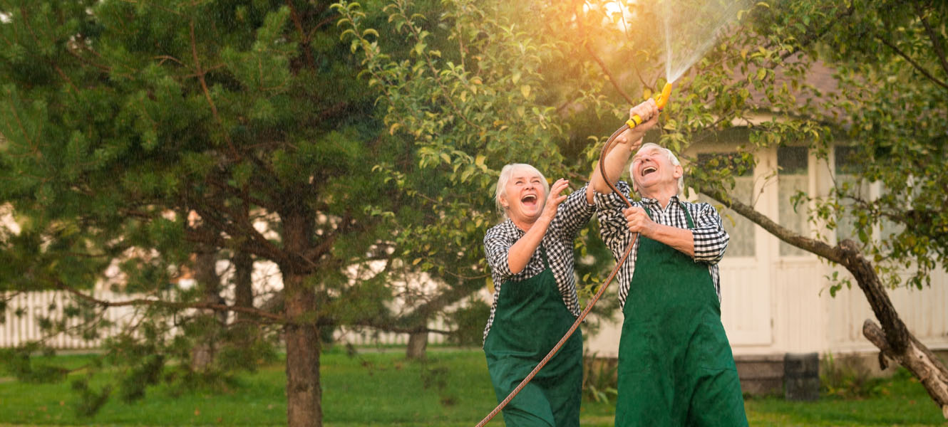 Husband and Wife playing with a water hose in their yard.